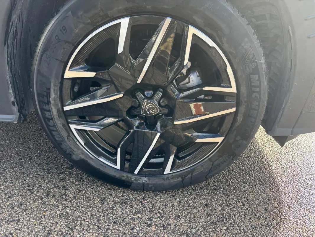 Gros plan sur la jante alliage noire et argent de 19 pouces du Peugeot 3008 Hybrid gris, avec pneu Michelin visible.