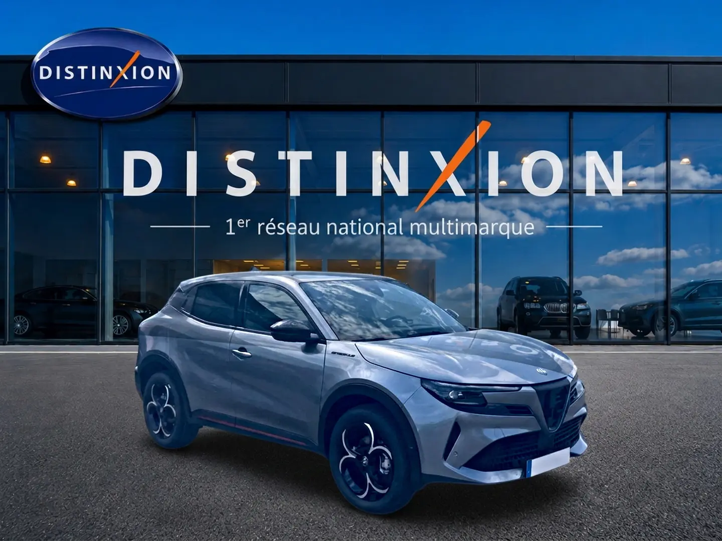 Vue 3/4 avant droite d'une Alfa Romeo Junior gris métallisé avec jantes en alliage et phares matrix LED devant un showroom Distinxion.