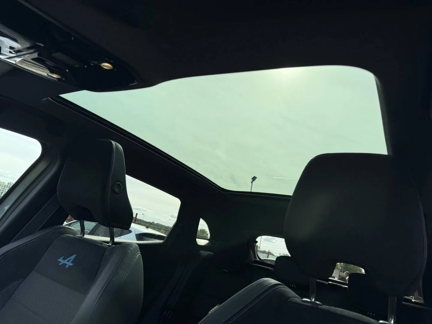 Vue intérieure du toit panoramique et des sièges avant noirs avec logo Alpine bleu sur Renault Austral 2026 gris satin.