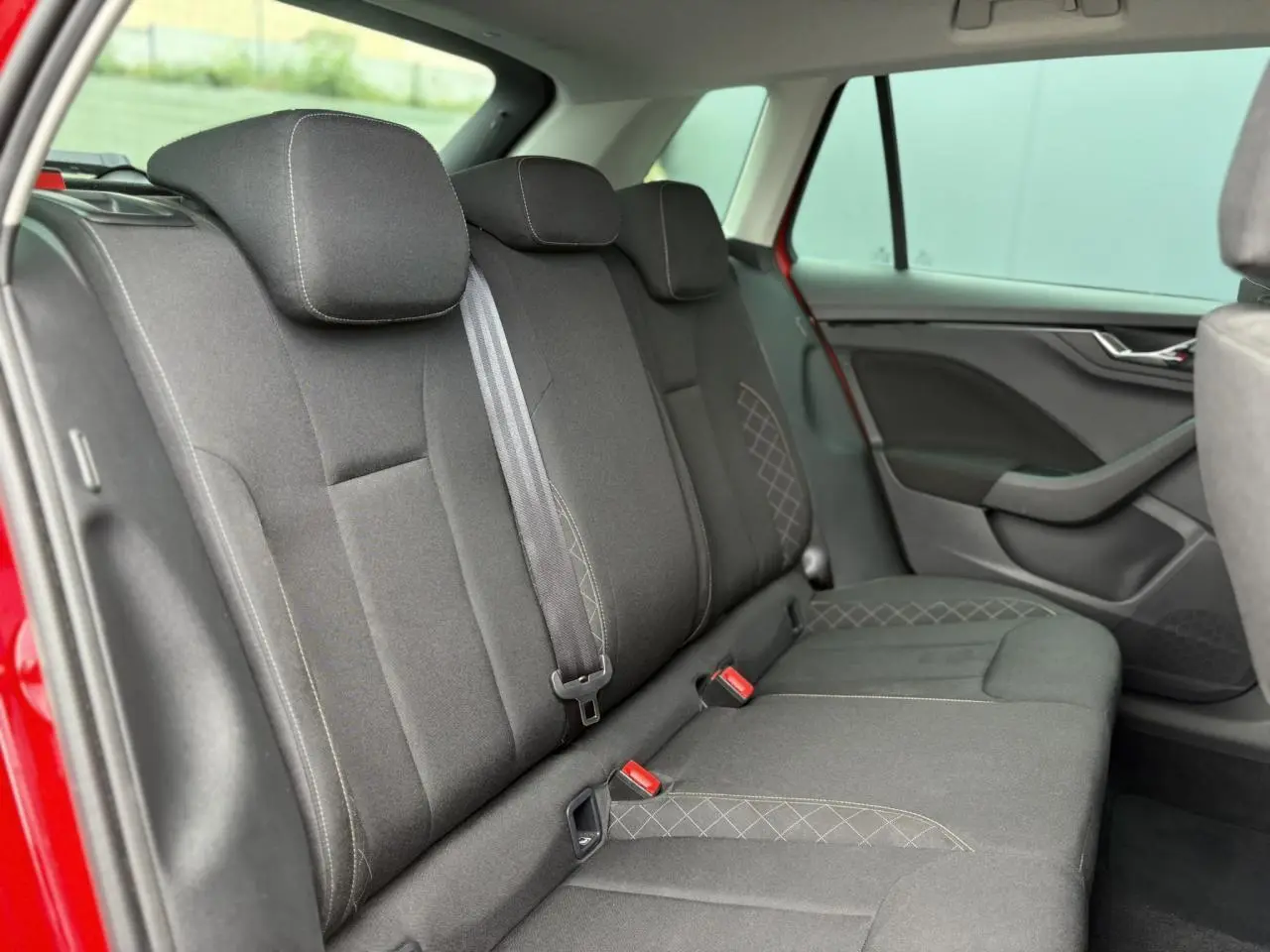 Vue intérieure du siège arrière côté droit d'une Skoda Kamiq rouge Velvet, avec sellerie tissu noire et surpiqûres grises.