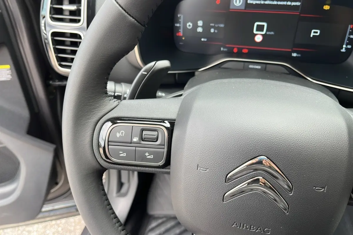 Gros plan sur le volant noir du Citroën C5 Aircross Hybrid 145, avec commandes intégrées et tableau de bord numérique visible.