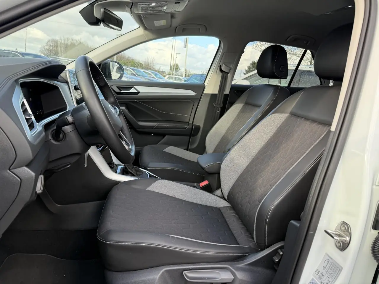 Intérieur côté conducteur du Volkswagen T-Roc blanc pur 2025, sièges bi-matière avec pack confort et volant cuir multifonction.