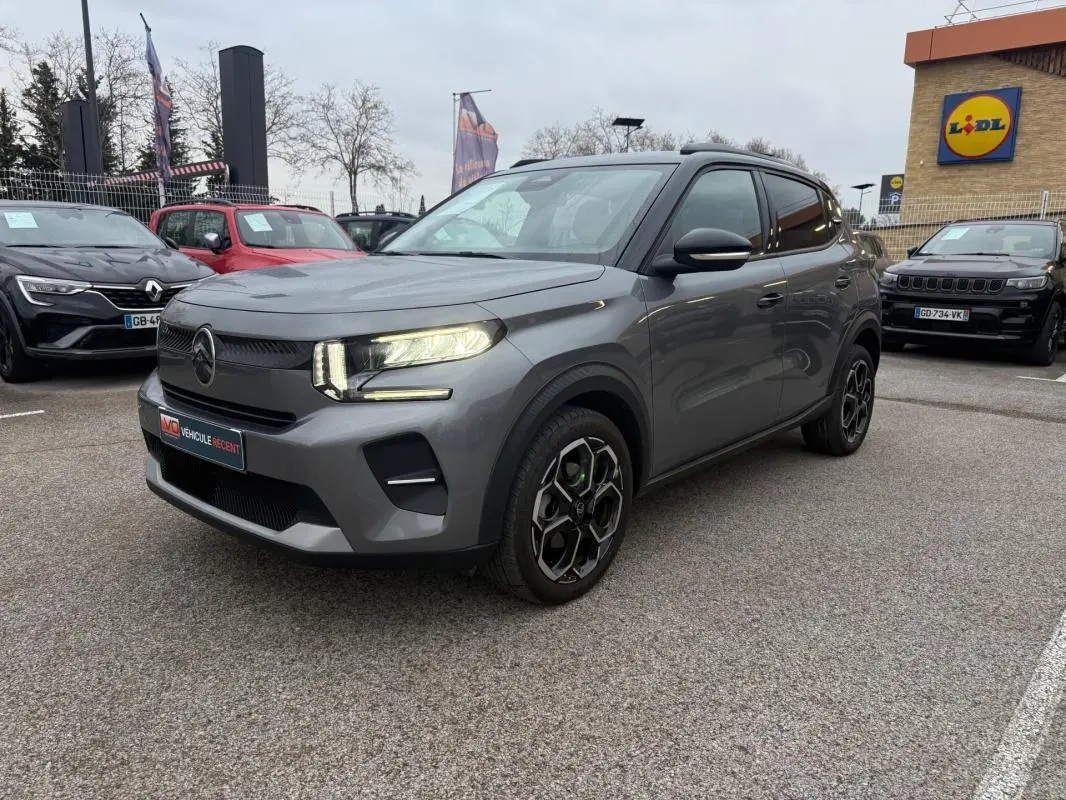 Citroën C3 gris vue 3/4 avant droit, avec jantes alliage noires et barres de toit visibles en extérieur.