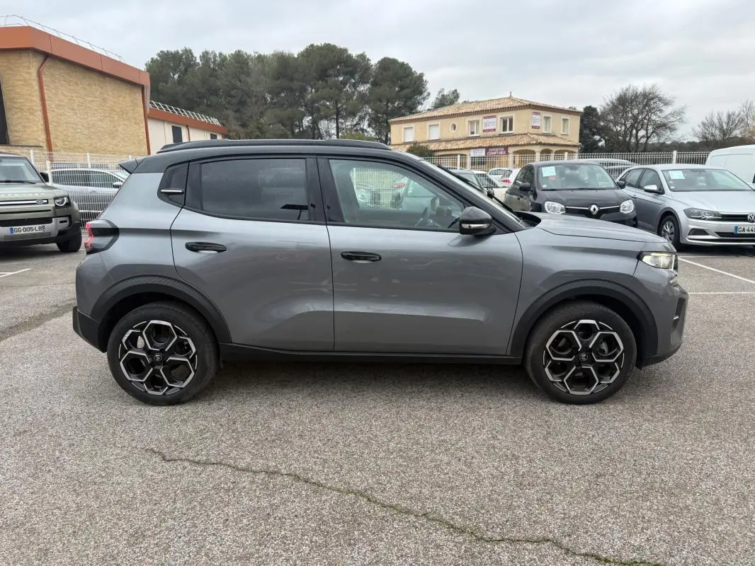 Vue latérale droite d'une Citroën C3 gris métallisé 2025 avec jantes alliage 17 pouces et barres de toit noires.
