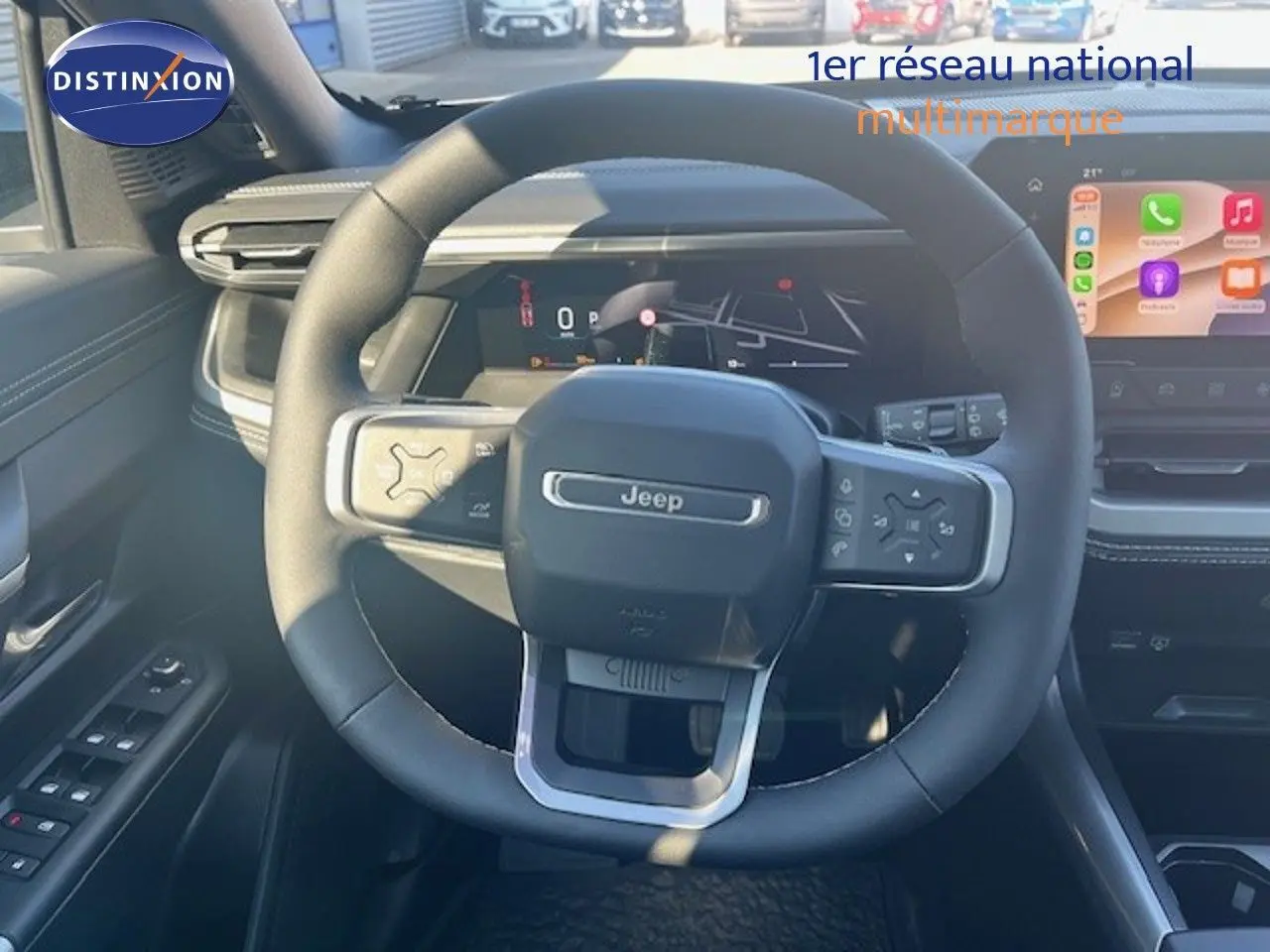 Vue intérieure centrée sur le volant Jeep noir avec tableau de bord numérique et écran tactile couleur.