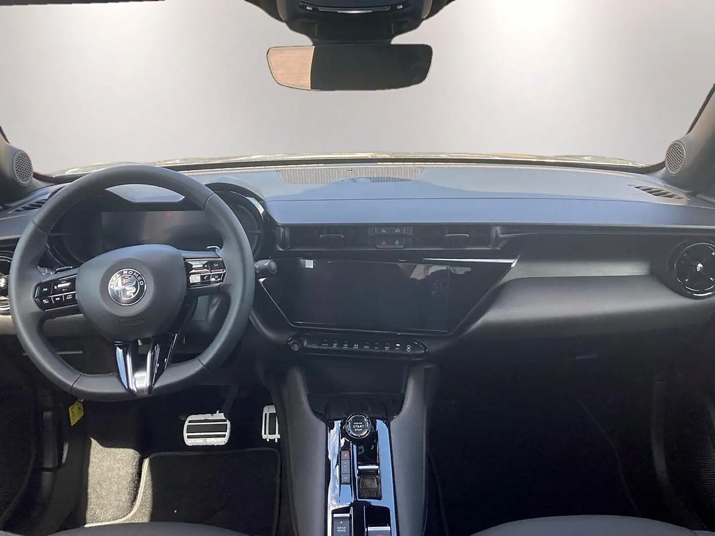 Vue intérieure frontale de l'Alfa Romeo Junior 1.2 hybride, tableau de bord noir avec écran tactile et volant multifonction.