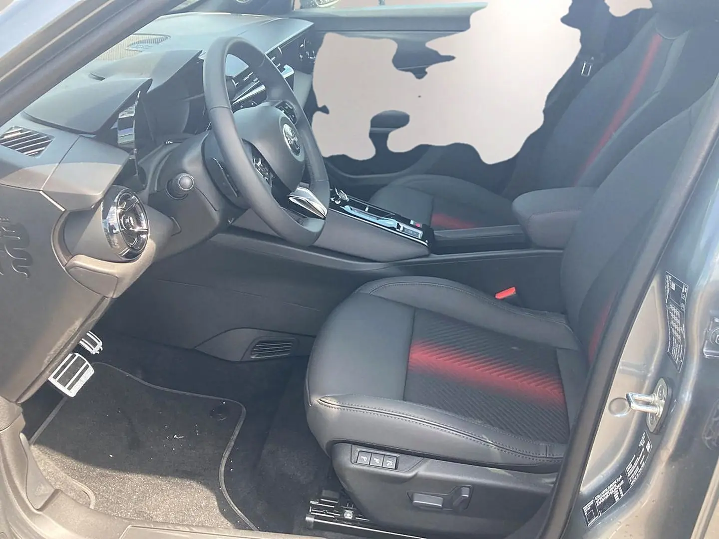 Vue intérieure côté conducteur de l'Alfa Romeo Junior gris, sièges noirs avec surpiqûres rouges et volant multifonction.
