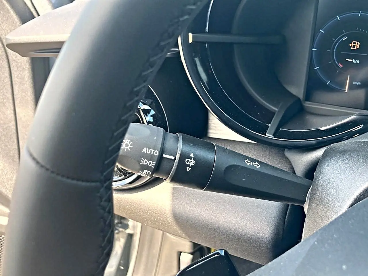 Gros plan sur le commodo gauche derrière le volant noir de l'Alfa Romeo Junior gris, avec tableau de bord partiellement visible.