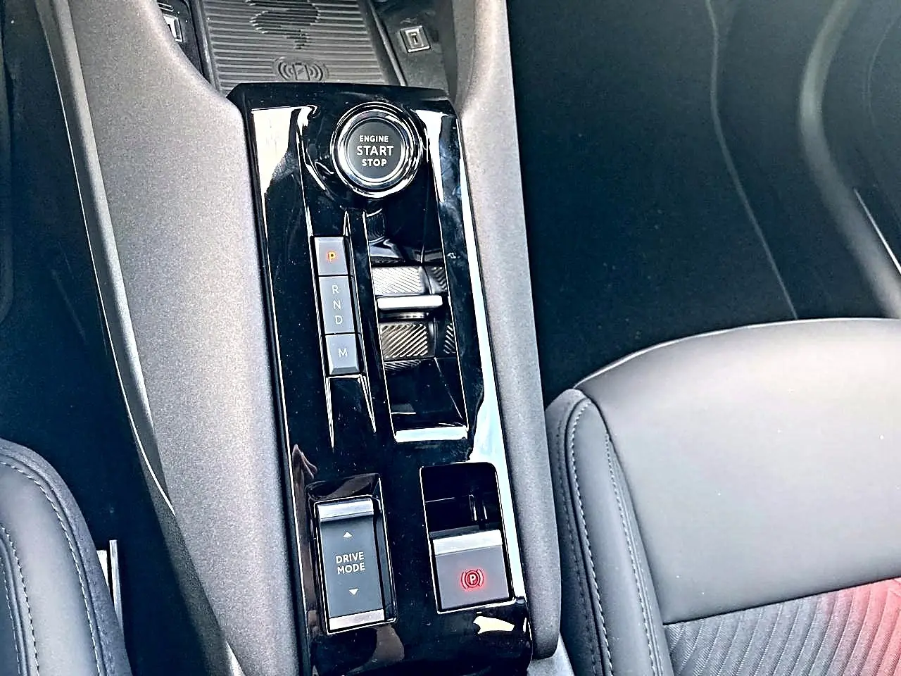 Gros plan sur la console centrale noire brillante de l'Alfa Romeo Junior 1.2 hybride, avec bouton start/stop et levier de vitesses.