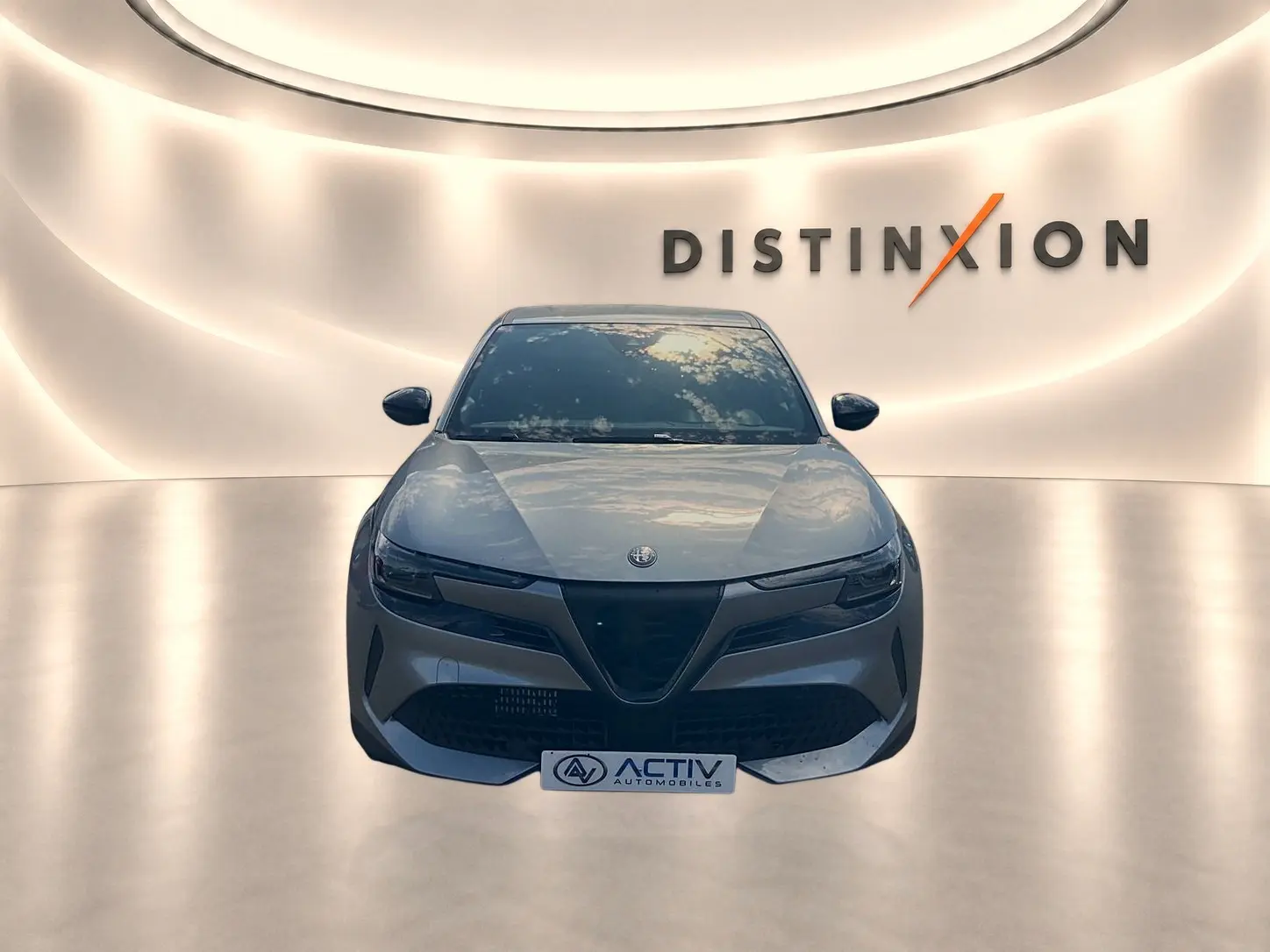 Vue frontale d'une Alfa Romeo Junior 1.2 hybride grise, avec calandre caractéristique et phares LED matrix allumés.