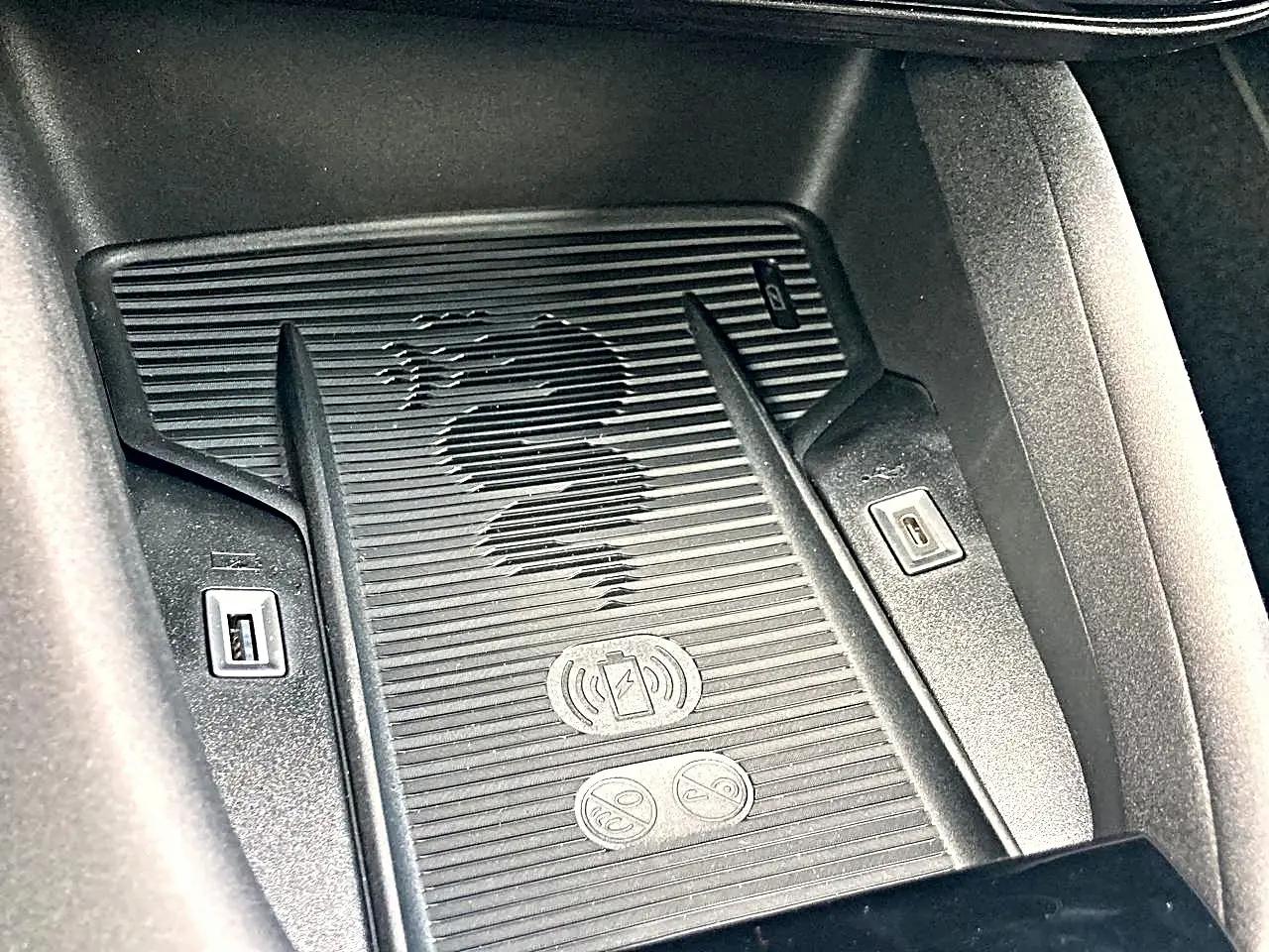 Détail du chargeur à induction noir avec logo serpent Alfa Romeo gravé, dans l’habitacle de l’Alfa Romeo Junior gris.