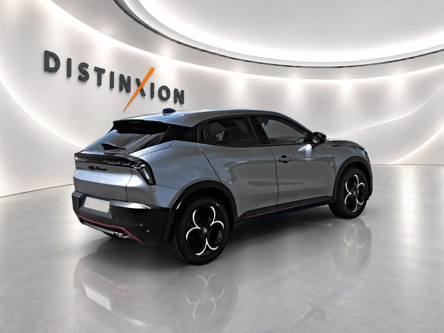 Vue 3/4 arrière droite d'une Alfa Romeo Junior gris métallisé avec jantes noires et toit noir dans un showroom lumineux.
