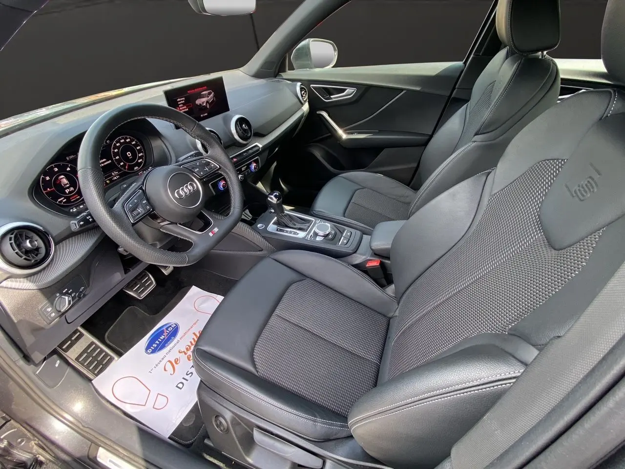 Vue intérieure côté conducteur de l'Audi Q2 35 TDI S-Line 2024 avec sièges cuir noir et volant sport multifonction.