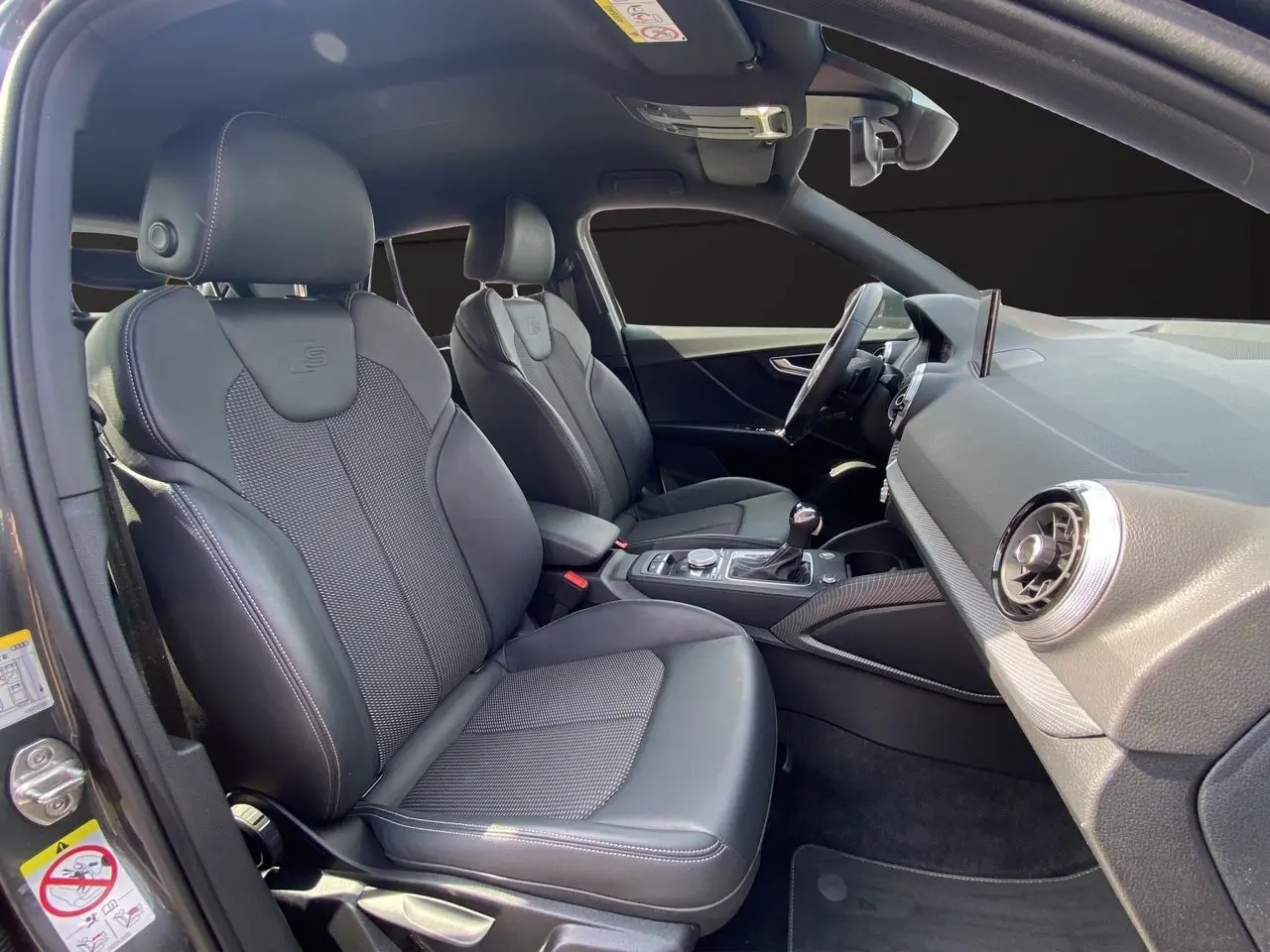 Vue intérieure côté conducteur de l'Audi Q2 S line 2024 avec sièges sport cuir et tableau de bord moderne.