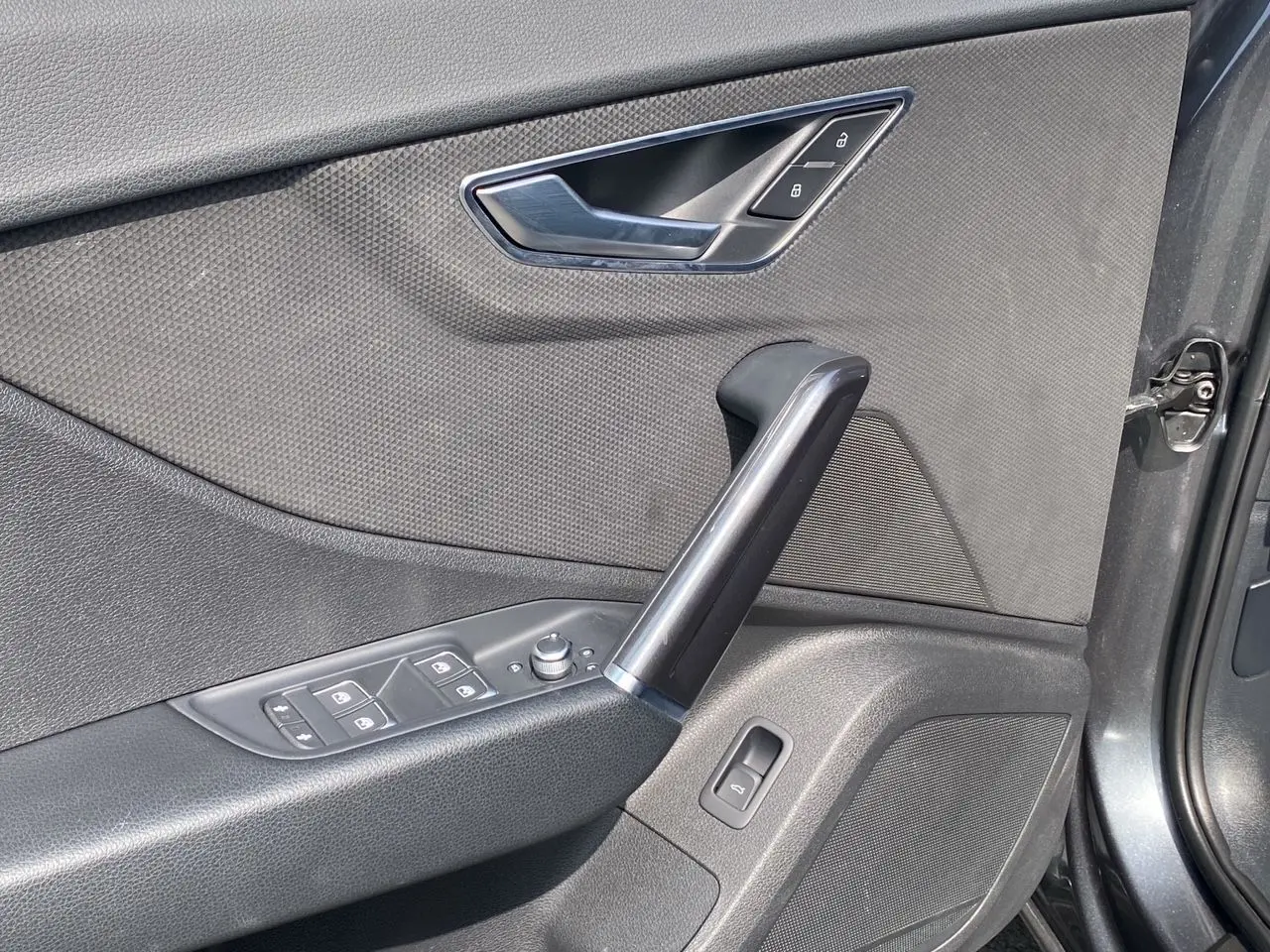 Gros plan sur la porte avant droite de l'Audi Q2 gris Daytona, montrant les commandes de vitres et la poignée intérieure noire.