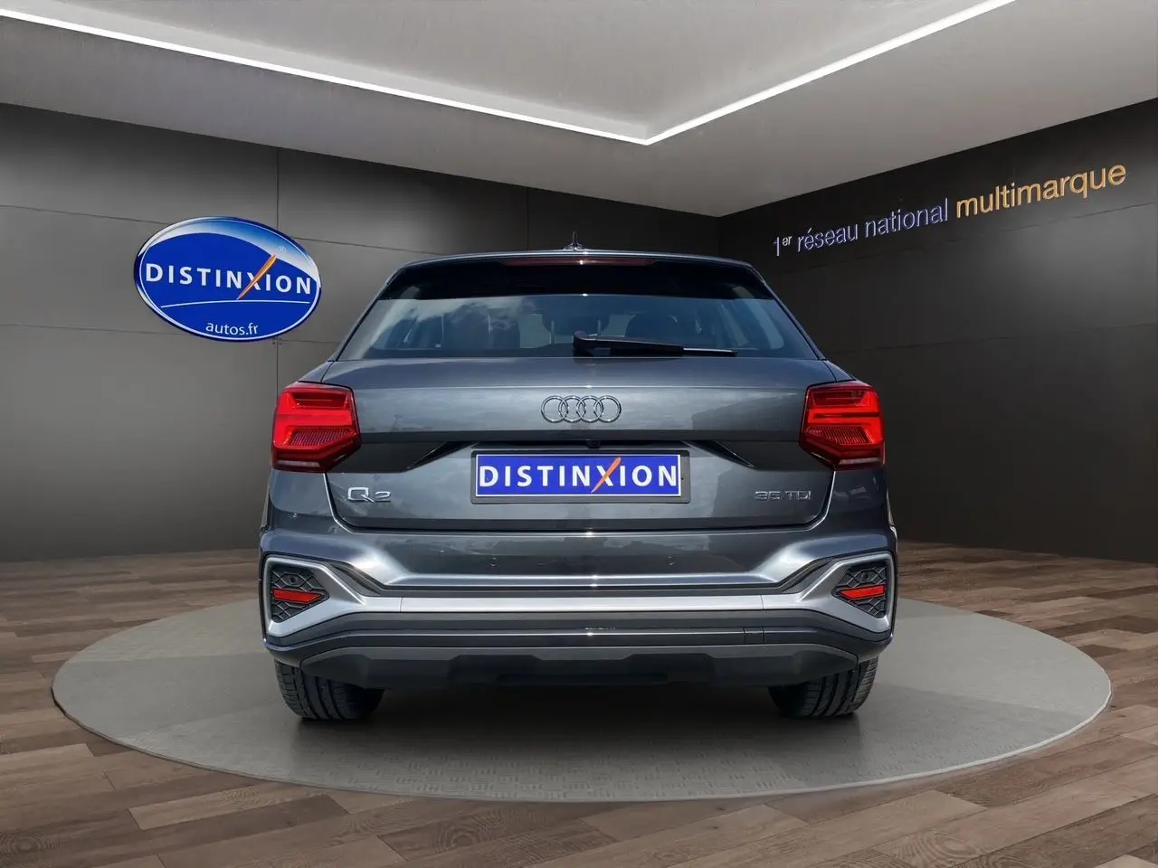 Vue arrière d'un Audi Q2 gris Daytona avec feux LED et logo S line visible sur un podium intérieur.