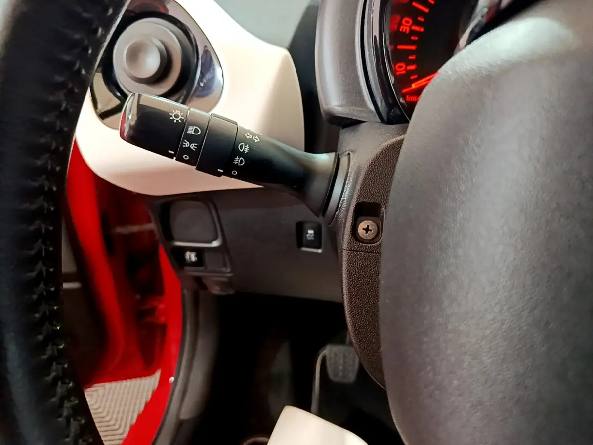 Détail du commodo d'éclairage à gauche du volant cuir dans l'habitacle rouge d'une Peugeot 108 2017.