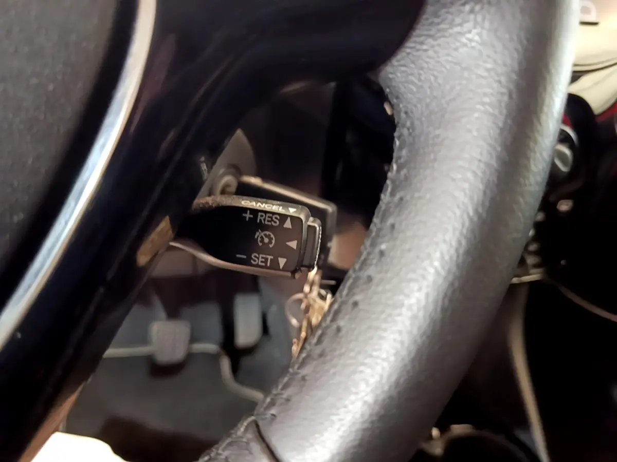 Gros plan sur le volant cuir noir de la Peugeot 108 rouge, avec commande de régulateur de vitesse visible.