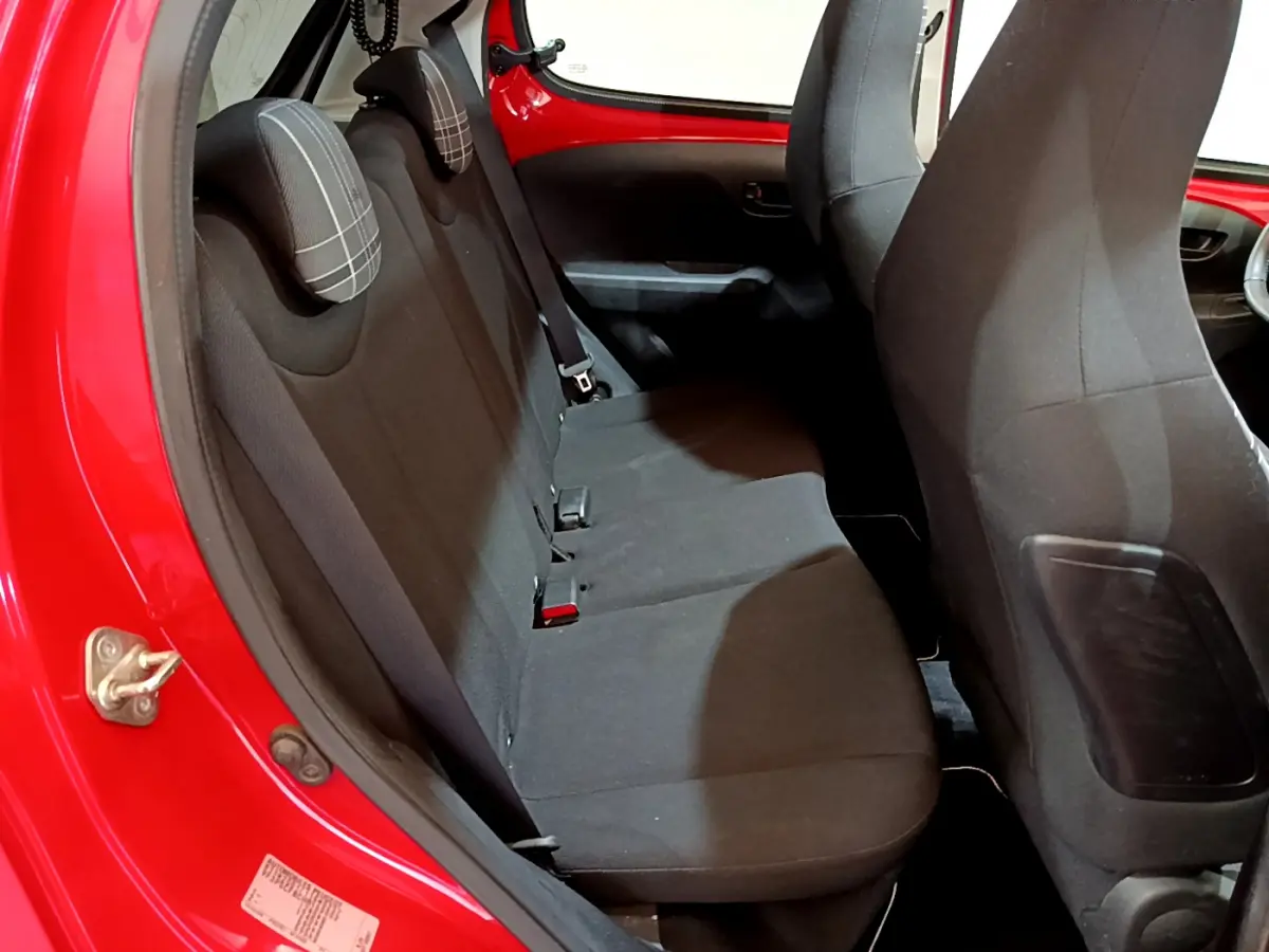 Vue intérieure côté gauche sur la banquette arrière noire d'une Peugeot 108 rouge avec appuie-têtes à carreaux.