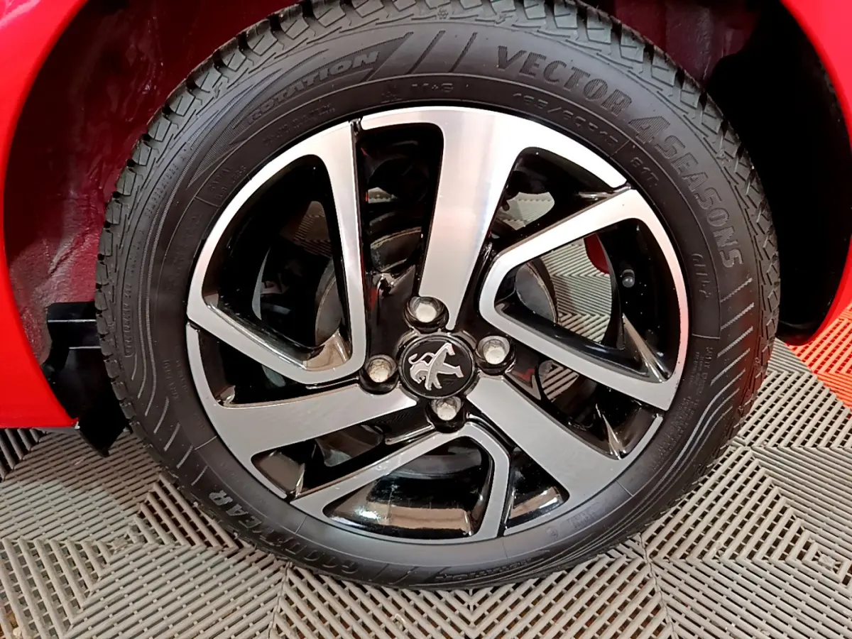 Gros plan sur la roue avant droite d'une Peugeot 108 rouge avec jante alliage bicolore et logo lion central.