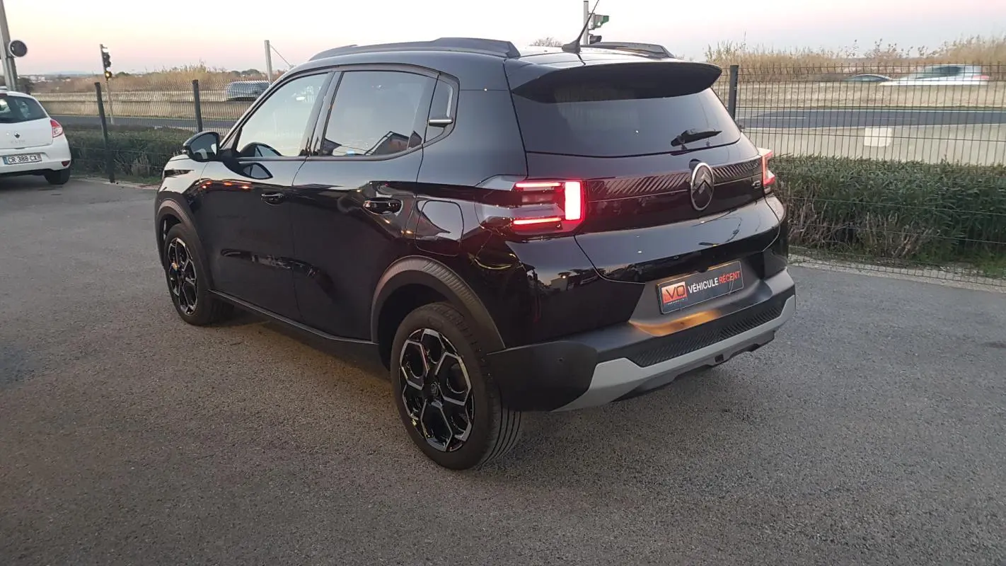 Vue 3/4 arrière droite d'une Citroën C3 noire 2025 avec jantes alliage 17 pouces et barres de toit.