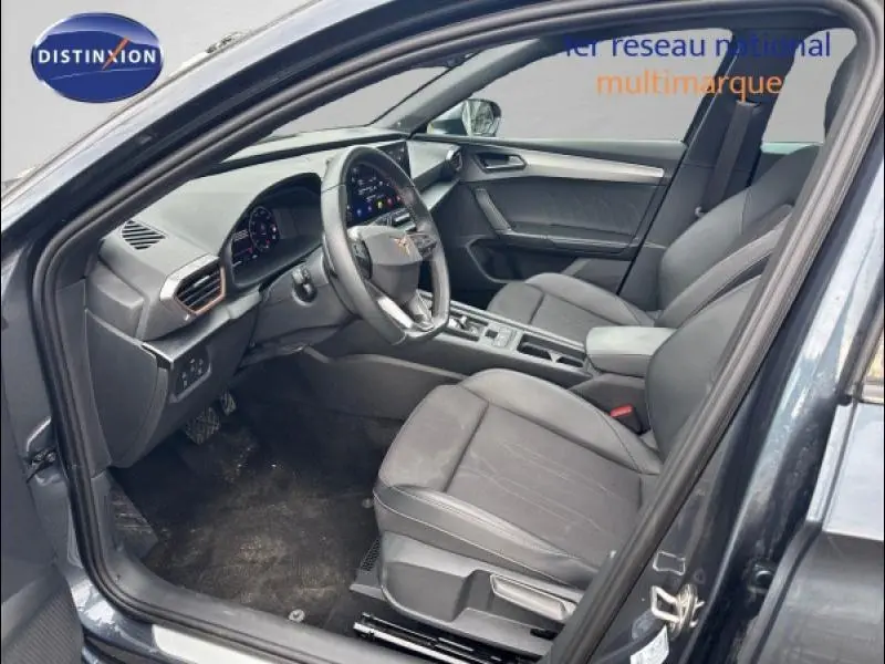 Intérieur avant droit de la CUPRA Leon 2024 gris Magnétique Mat, sièges tissu noir et volant cuir multifonction.