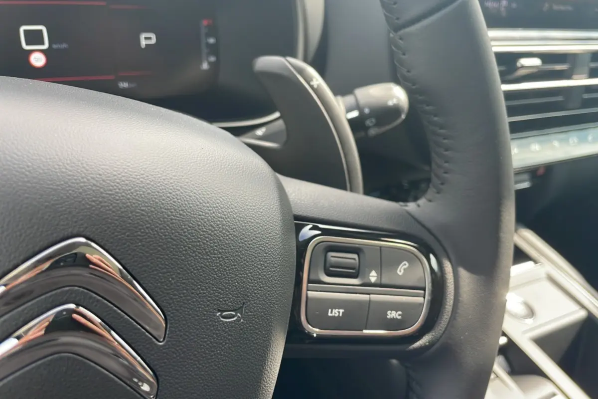 Gros plan sur le volant noir du Citroën C5 Aircross Hybrid 2025 avec commandes intégrées et palettes au volant.