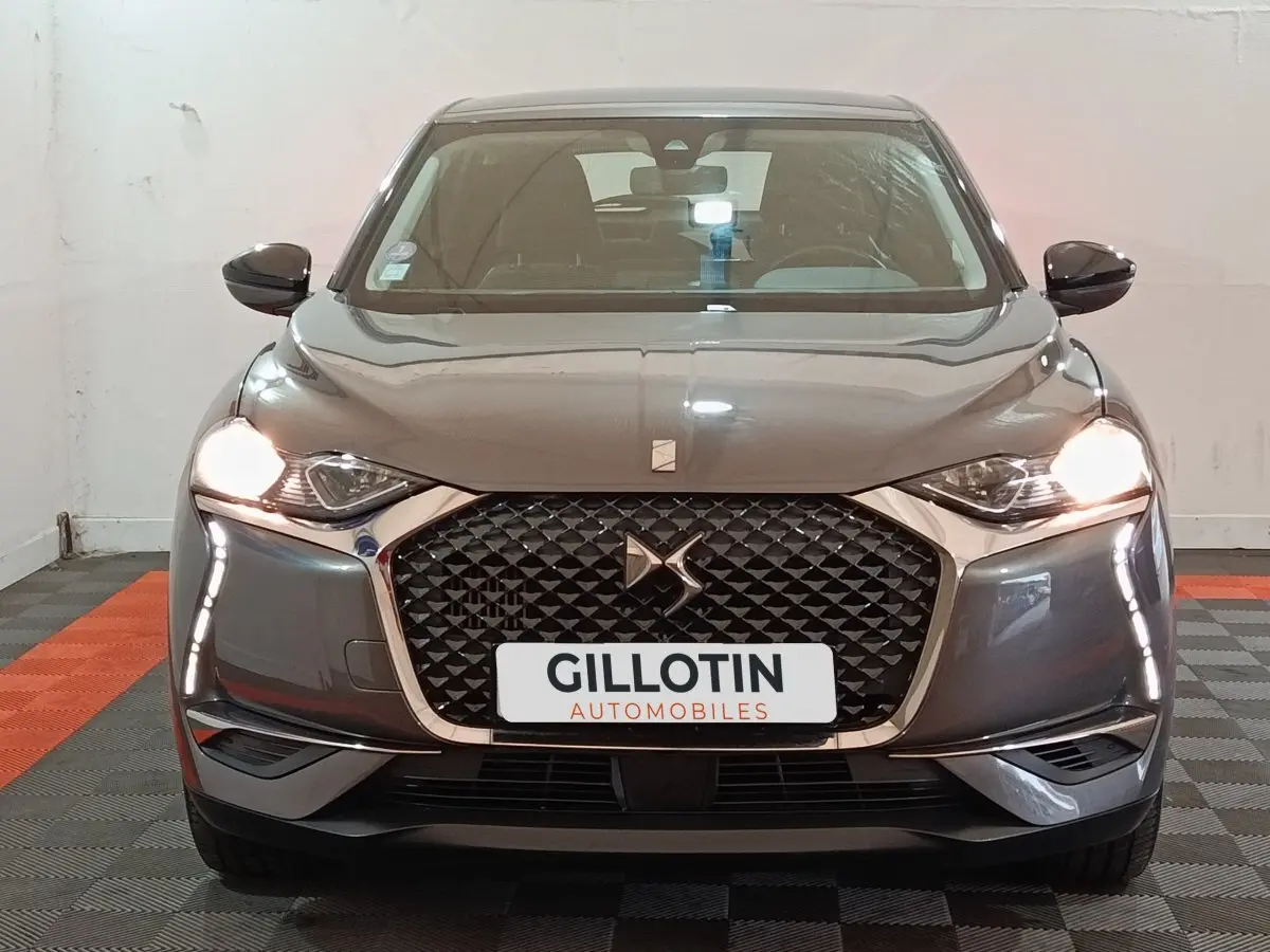 Vue frontale d'un DS3 Crossback gris foncé avec calandre distinctive et phares allumés en intérieur.