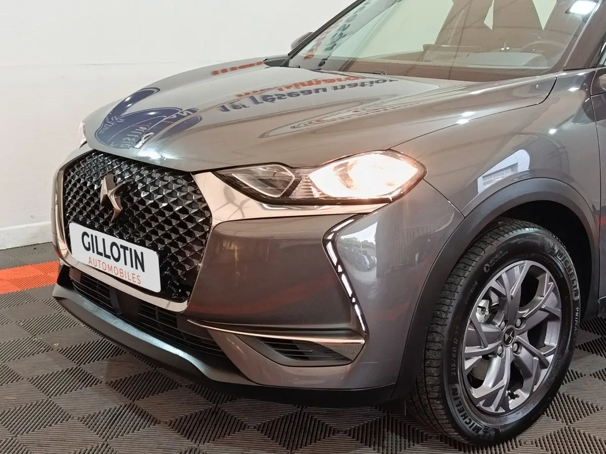 Vue 3/4 avant droit du DS3 Crossback gris foncé avec phares allumés et calandre distinctive en losange noir.