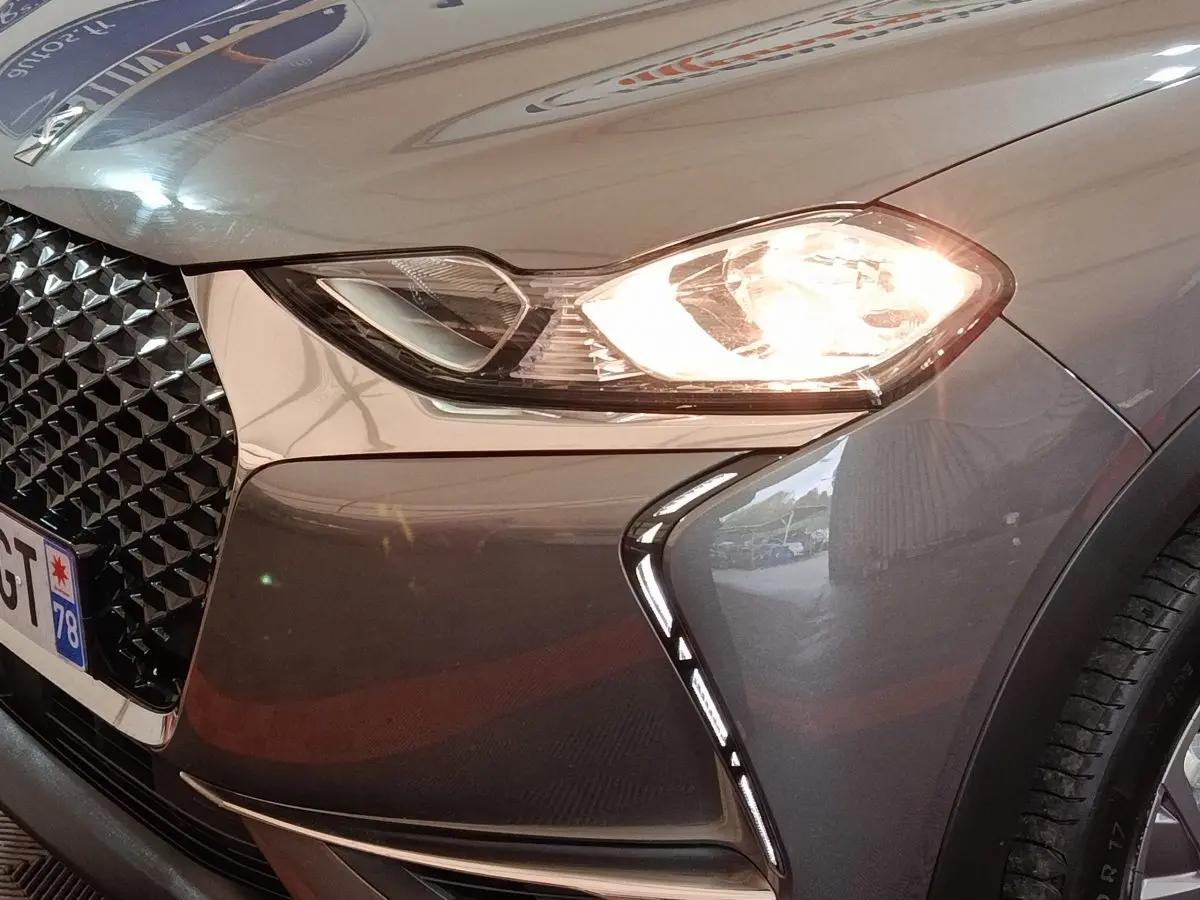 Gros plan sur l'avant droit gris foncé du DS3 Crossback avec phare allumé et calandre distinctive noire.