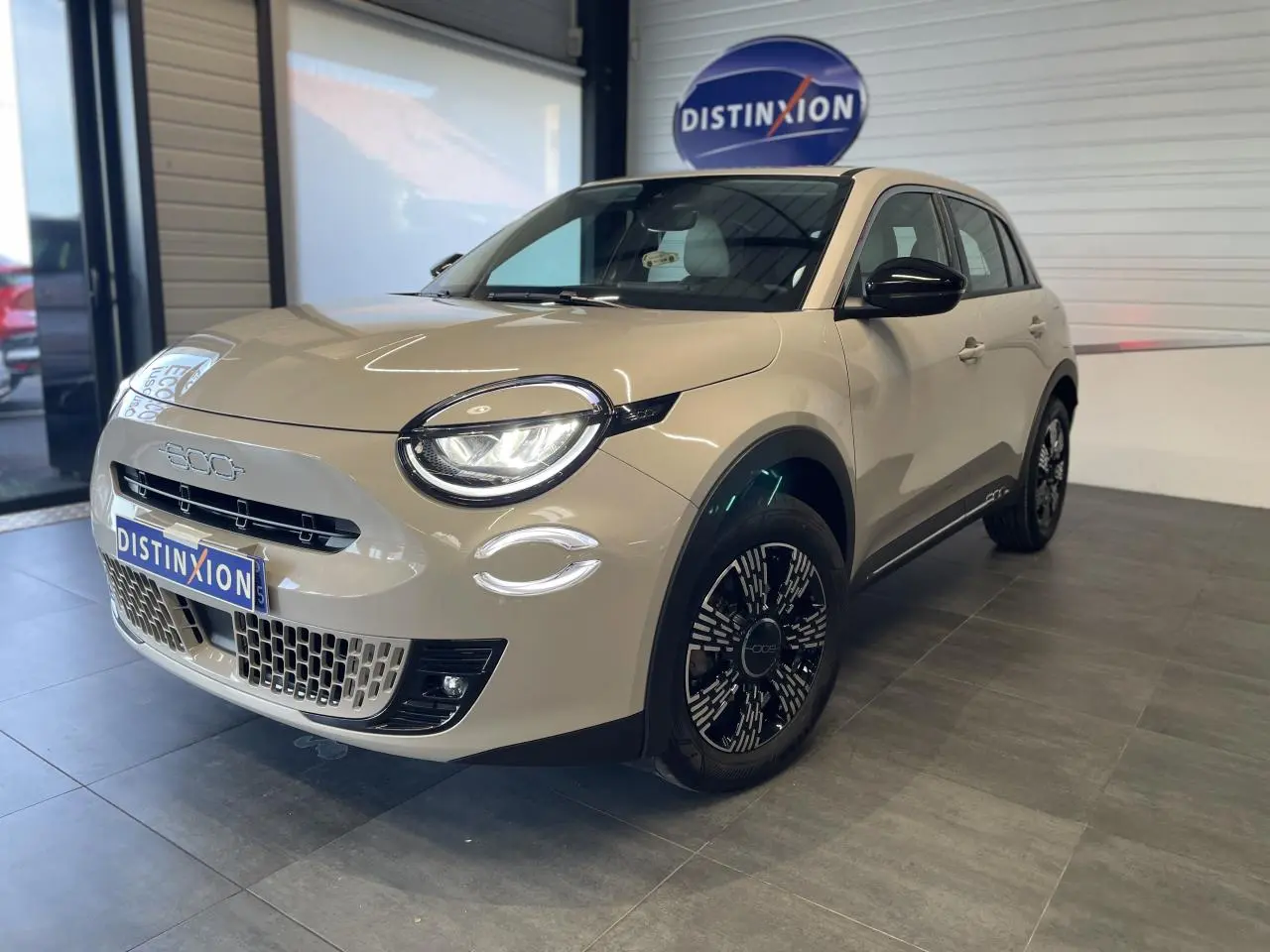 Vue 3/4 avant droit d'une FIAT 600 beige métallisé avec jantes alliage noires et détails chromés showroom.