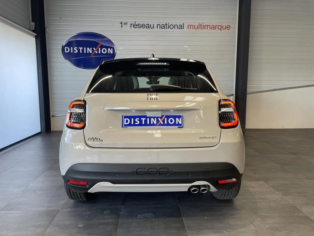 Vue arrière d'une FIAT 600 beige métallisé avec double sortie d'échappement côté droit et feux arrière LED allumés.