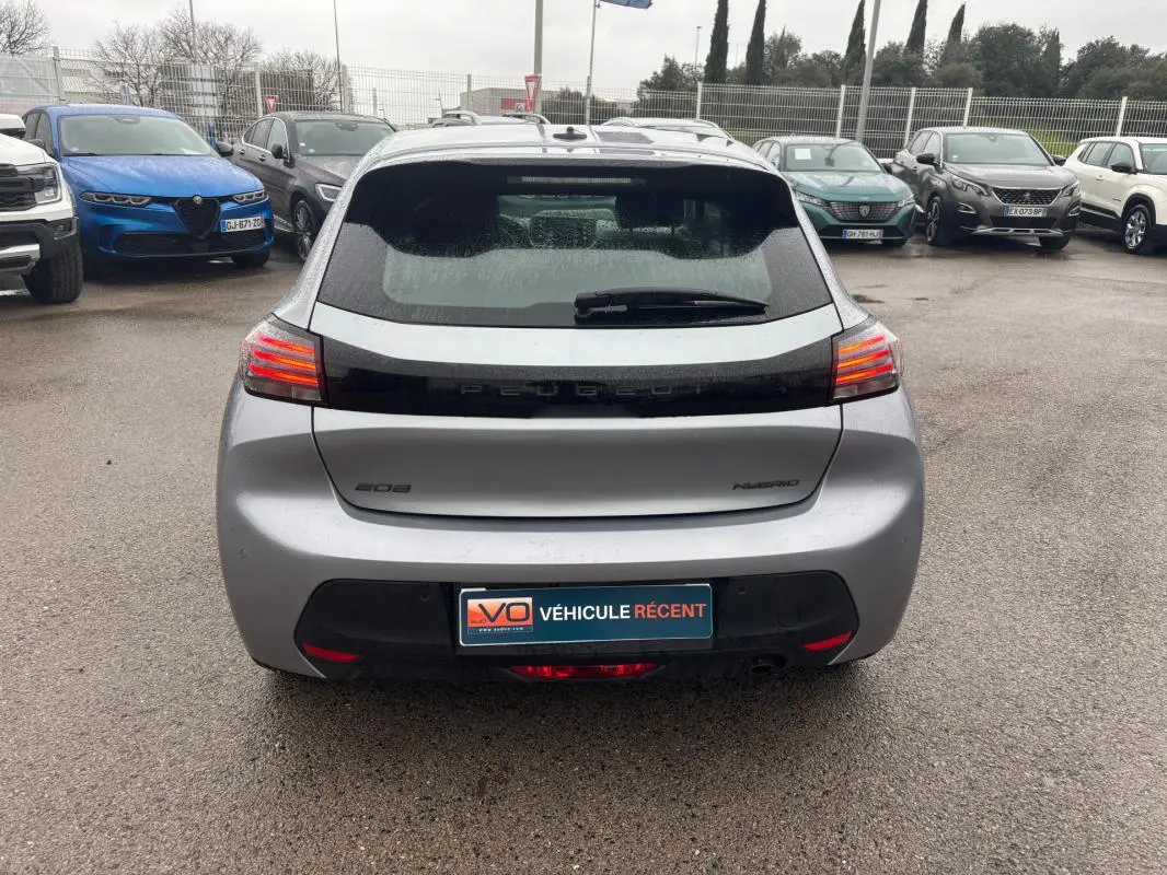 Vue arrière d'une Peugeot 208 Hybrid 100 e-DCS6 Style gris, avec feux arrière allumés sur parking humide.