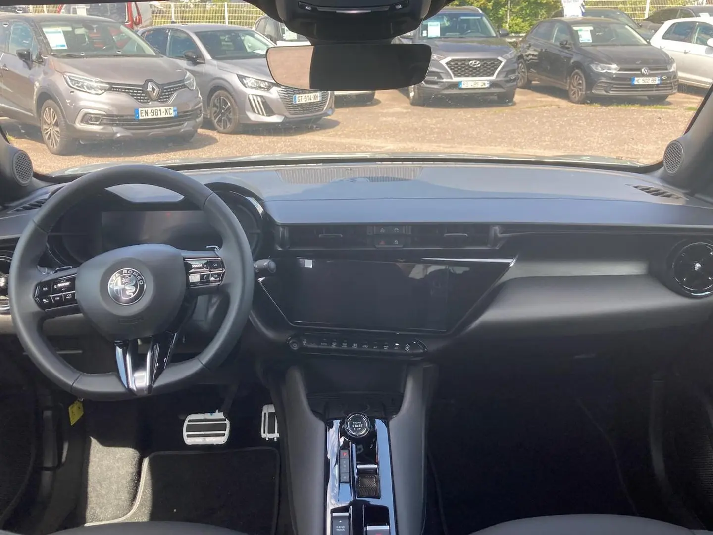 Vue intérieure avant de l'Alfa Romeo Junior 1.2 hybride grise, tableau de bord épuré avec écran tactile et volant multifonction.