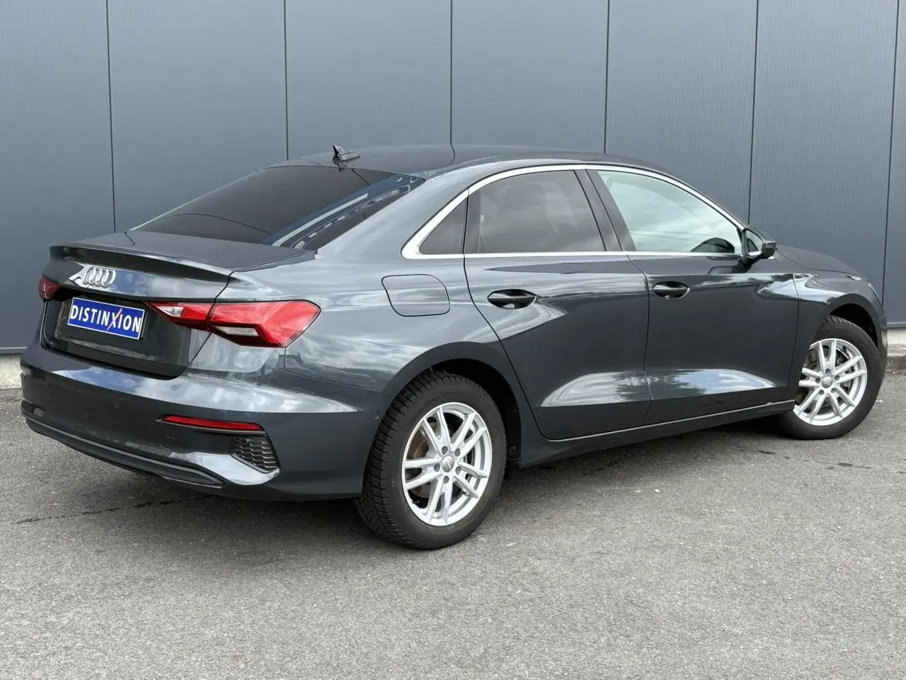 Audi A3 Berline gris métallisé vue 3/4 arrière droit avec vitres surteintées et jantes argentées.