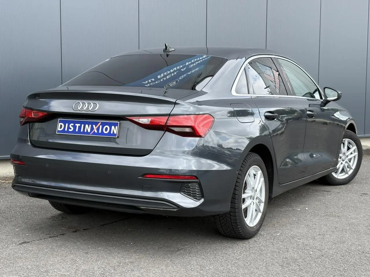 Audi A3 Berline gris métallisé vue 3/4 arrière droit avec vitres surteintées et jantes argentées.