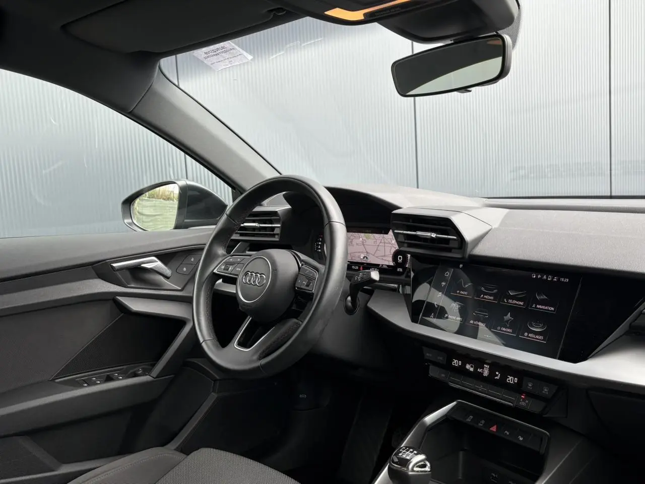 Intérieur Audi A3 Berline gris, vue côté conducteur, volant cuir multifonctions et écran tactile MMI visible.