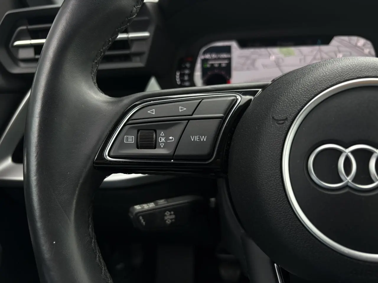Gros plan sur le volant cuir noir multifonctions de l'Audi A3 Berline 35 TFSI 2020 avec affichage numérique en arrière-plan.