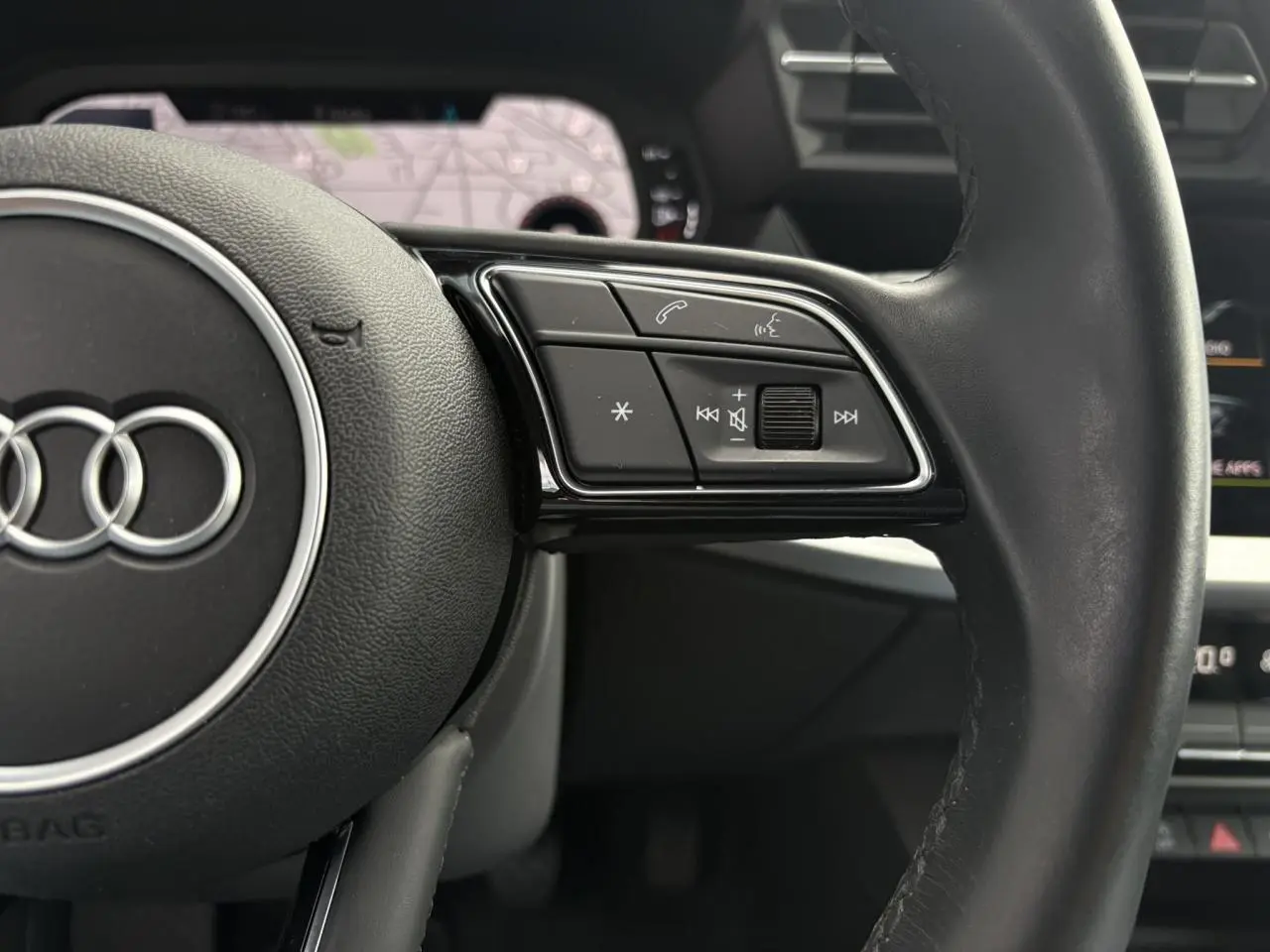 Gros plan sur le volant cuir noir multifonctions de l'Audi A3 Berline 35 TFSI 150 Design avec écran GPS en arrière-plan.