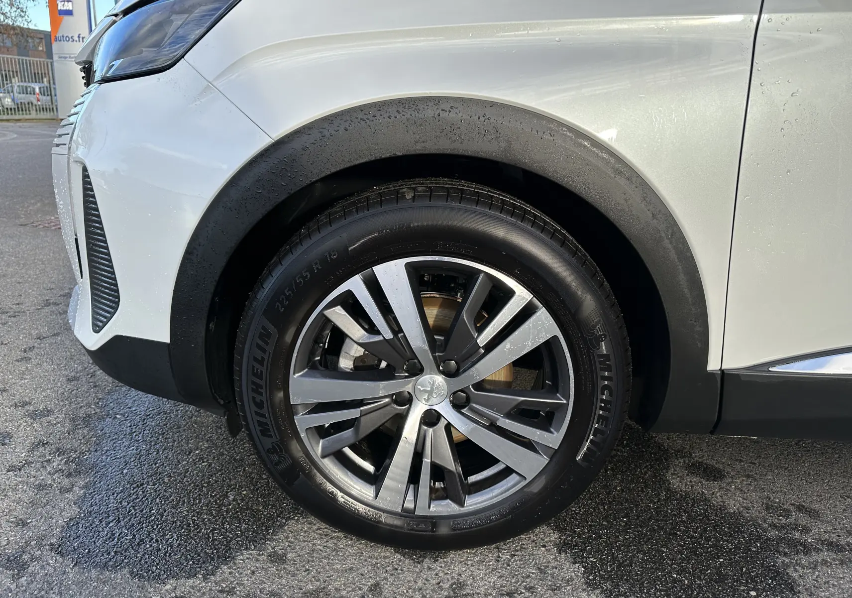 Gros plan sur la roue avant gauche d'un Peugeot 3008 blanc nacré, mettant en valeur la jante alliage et le pneu Michelin.