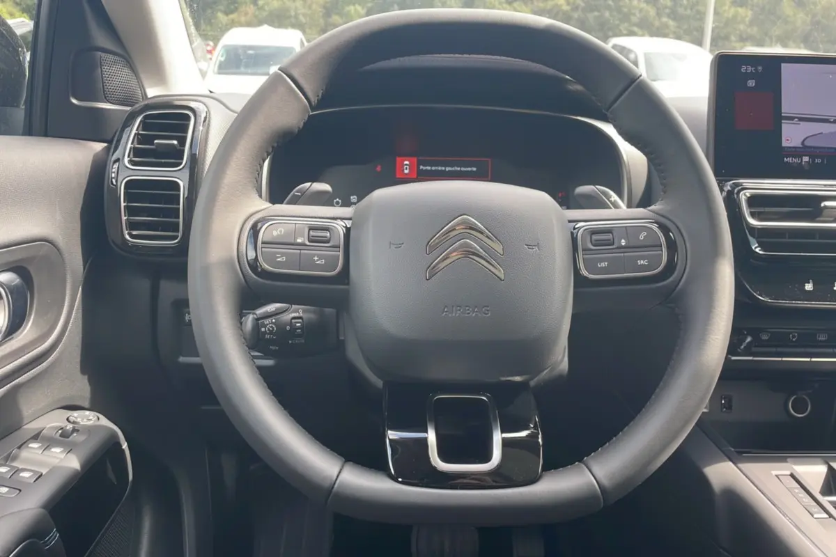 Vue intérieure centrée sur le volant du Citroën C5 Aircross Hybrid 2025, avec tableau de bord numérique et commandes au volant.