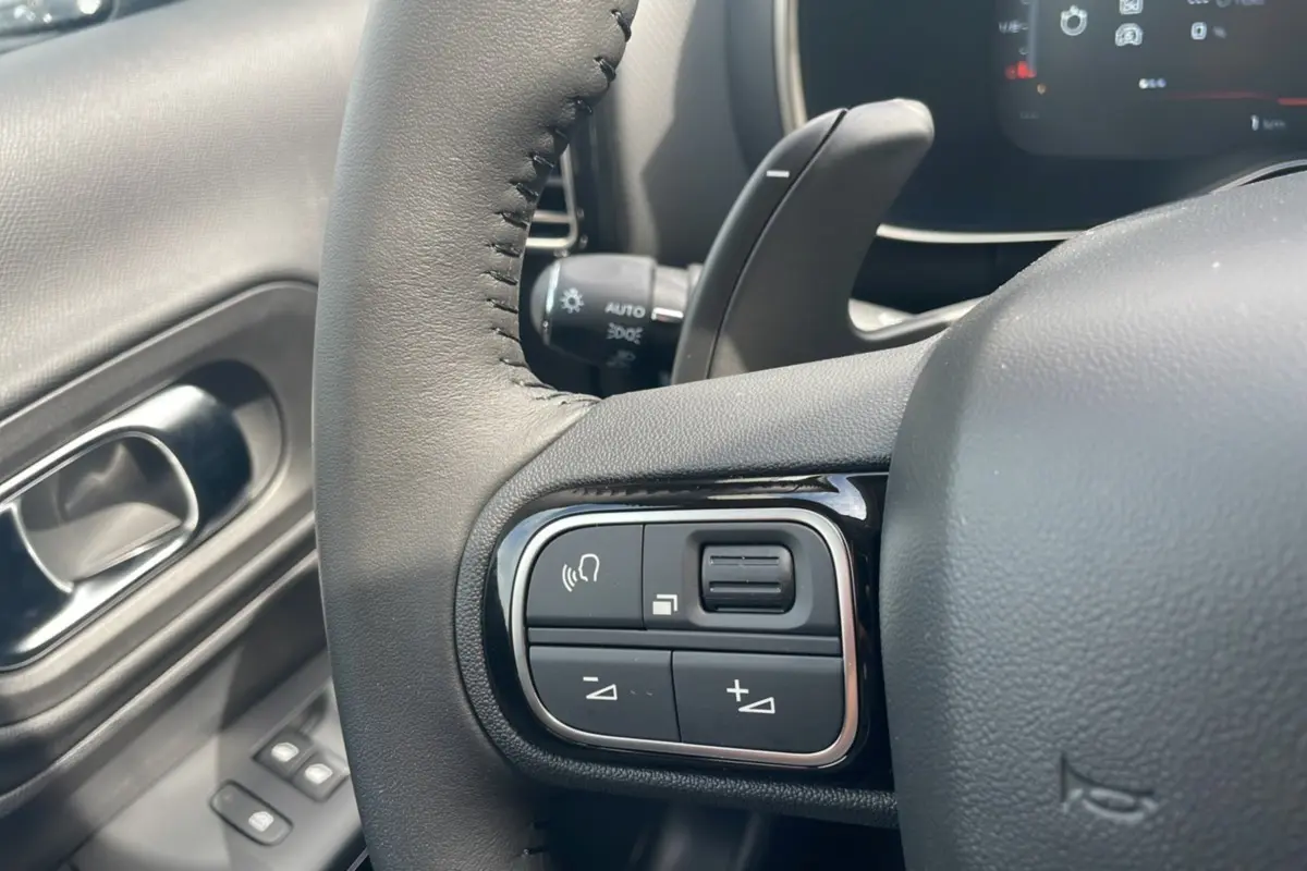 Gros plan sur les commandes du volant côté gauche du Citroën C5 Aircross Hybrid blanc avec toit noir, modèle 2025.