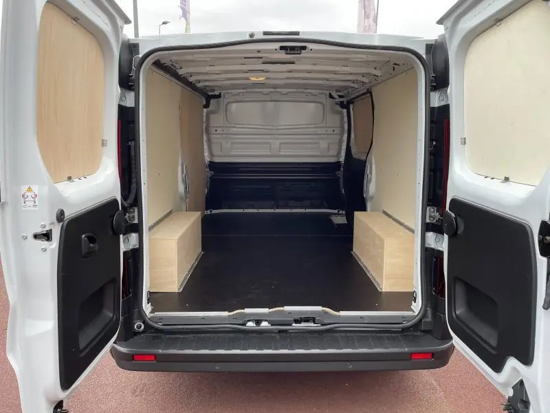 Vue arrière ouverte du Renault Trafic Fourgon blanc Glacier L2H1 2024, montrant l’espace de chargement avec habillage bois.