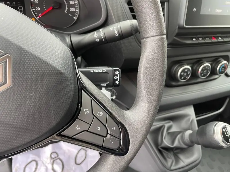 Gros plan sur le volant et la console centrale du Renault Trafic Fourgon blanc, avec commandes au volant et levier de vitesses manuel visible.