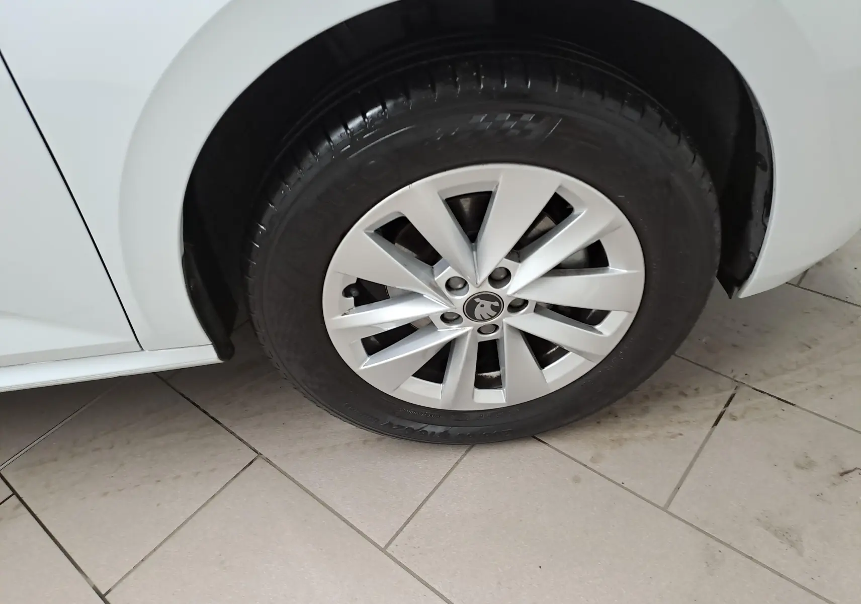 Gros plan sur la roue avant gauche d’un Skoda Kamiq blanc Lune, mettant en valeur la jante alliage et le logo central.