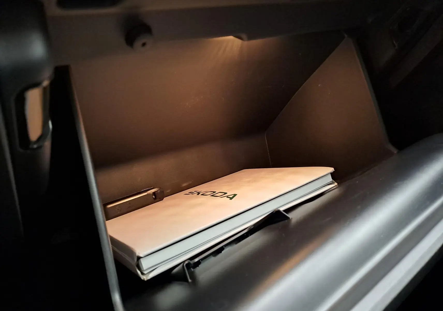 Vue intérieure du vide-poche côté passager du Skoda Kamiq blanc Lune avec manuel du véhicule posé à l'intérieur.