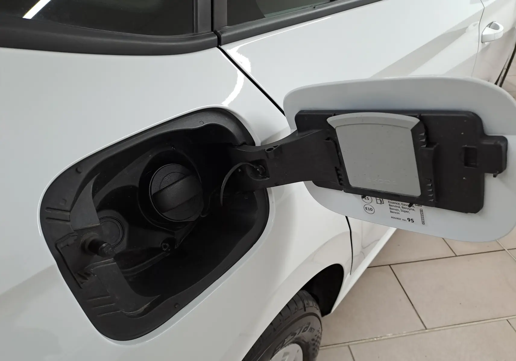 Gros plan sur la trappe à carburant côté gauche d’un Skoda Kamiq blanc Lune, essence, avec bouchon ouvert.