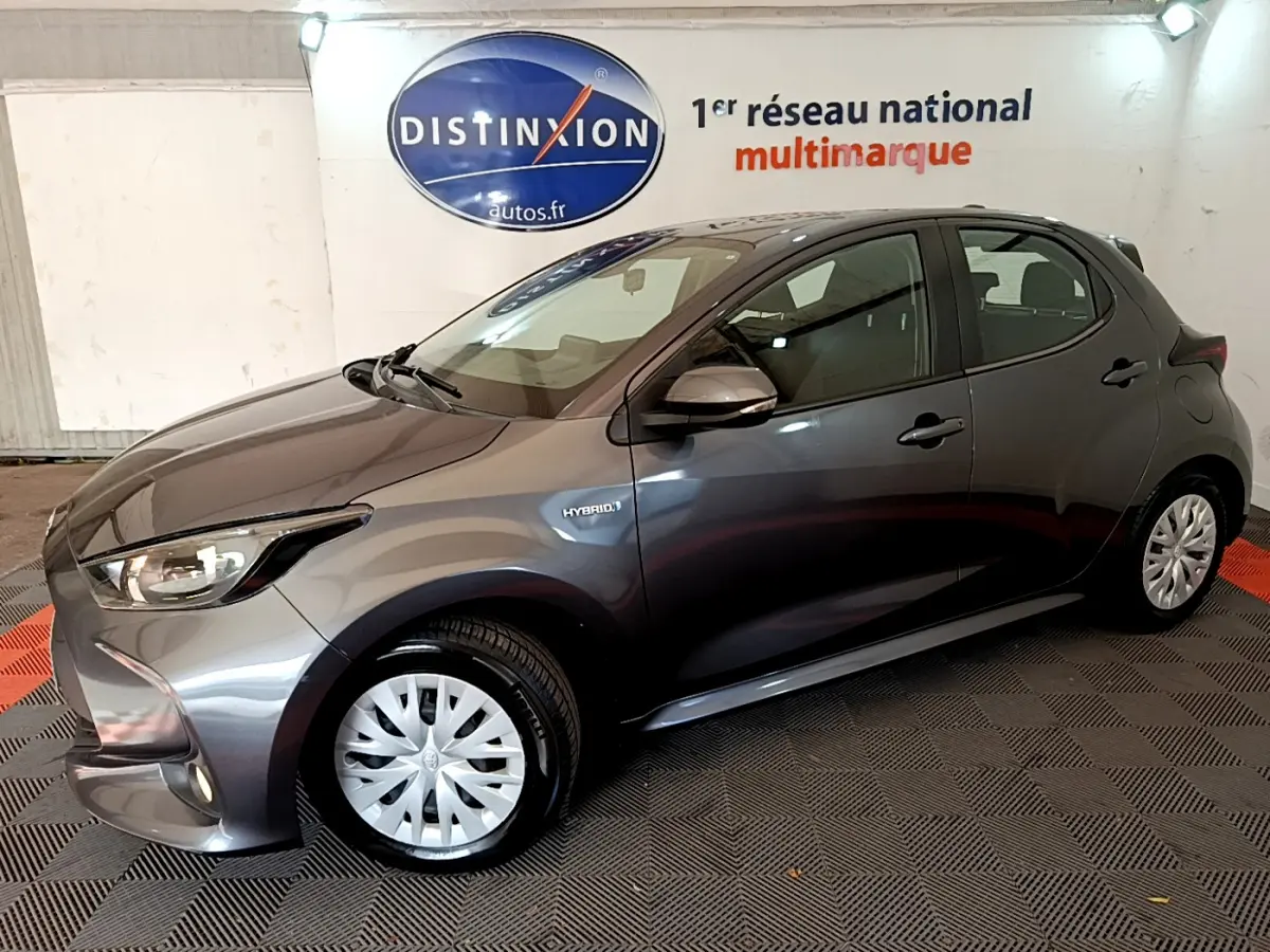 Toyota Yaris hybride gris clair vue de profil côté gauche, avec badge Hybrid et feux avant allumés.