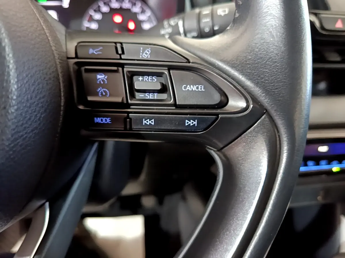 Gros plan sur les commandes du volant cuir de la Toyota Yaris hybride 2021, avec boutons de régulateur et assistance.