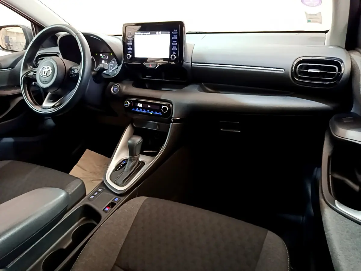Intérieur avant de la Toyota Yaris Hybride 116h 2021, tableau de bord noir avec écran tactile central et volant cuir multifonctions.